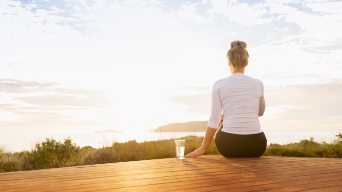 Women sitting on deck drinking water gazing toward horizon where the sun is shining