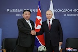 Kim Jong Un and Vladimir Putin shake hands in front of two flags.