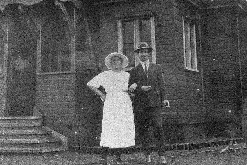 A black-and-white image of a couple in formal attire standing in front of a church.