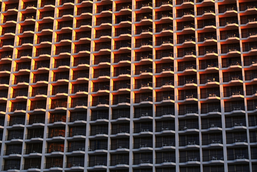 sunset view of a high-rise building with many balconies and a shadow cast over the lower floors by adjacent building