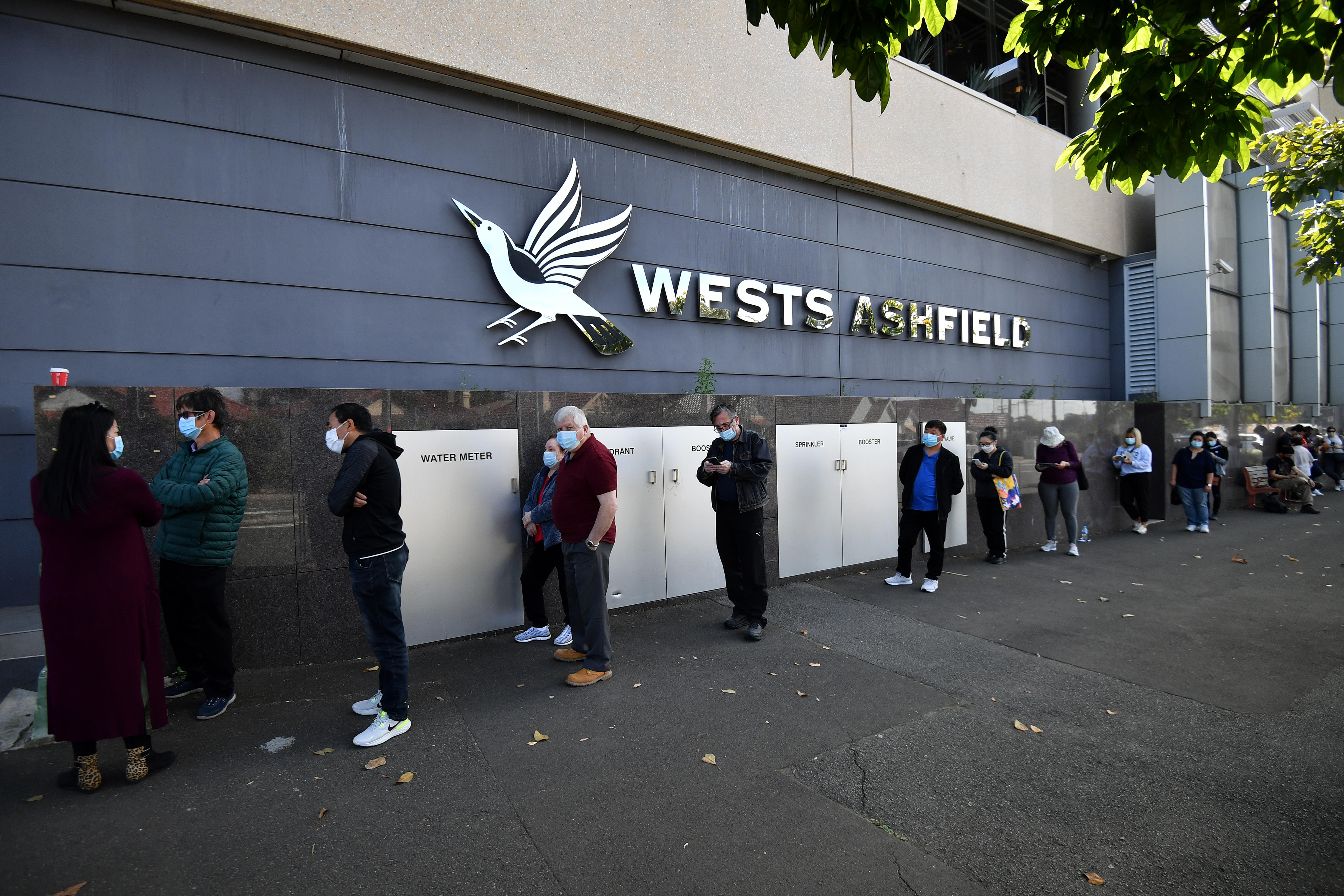 people in masks lining up outside a building reading wests ashfield