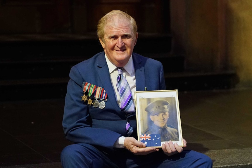 Graham Reed wears his gather's medals and holds his photo at the Anzac Day parade