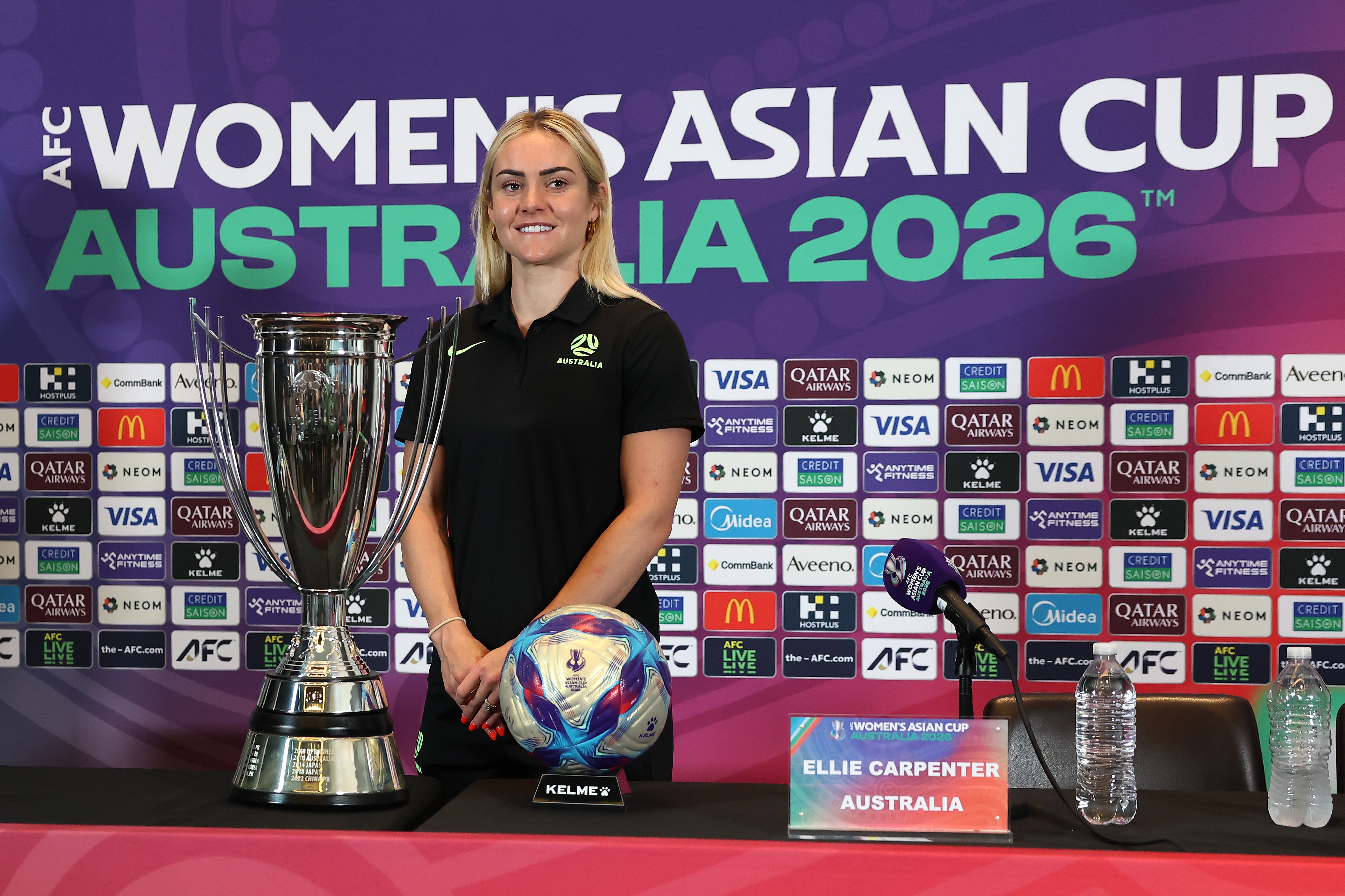 A vice-capitã do Matildas, Ellie Carpenter, sorri e posa atrás do troféu da Copa Asiática Feminina e de uma bola