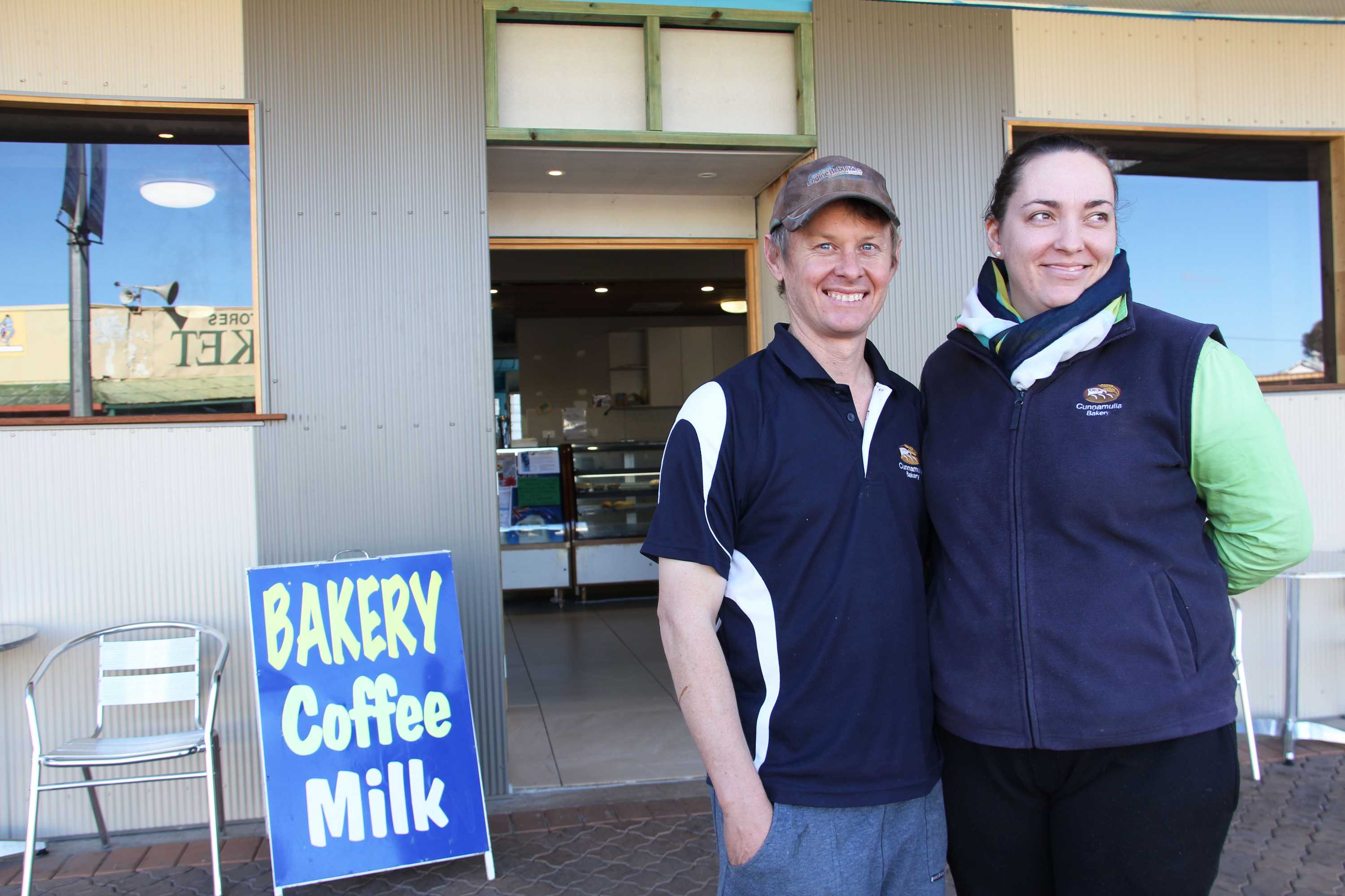 A man and a woman smiling in front of a bakery.