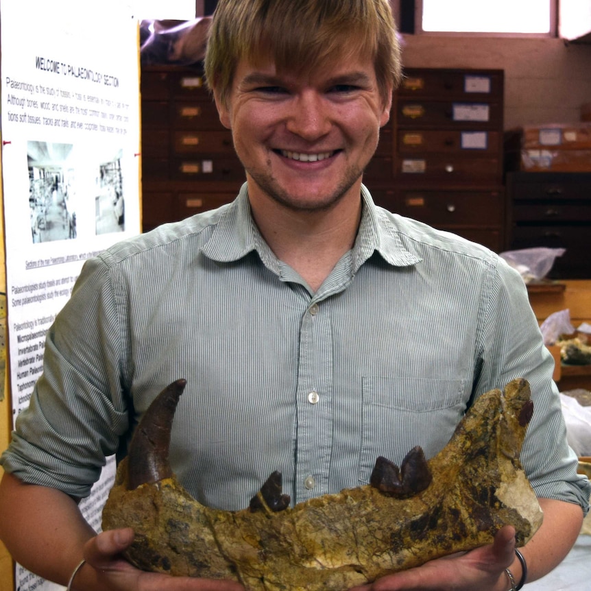 A smiling young man holds a large jawbone across his stomach.