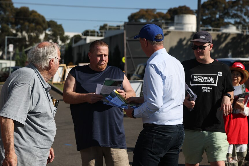 A man in a singlet receiving a pamphlet from volunteers at a prepolling booth in Noble Park.