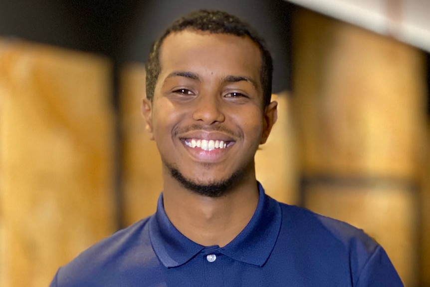 A smiling Abdi Ismail, wearing a blue cohealth-branded t-shirt.