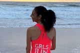 A woman stands on the beach facing the water with her running gear on.