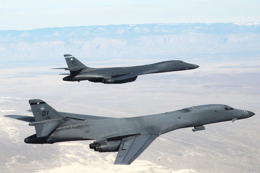 Two B-1B Lancers fly in formation over arid terrain.