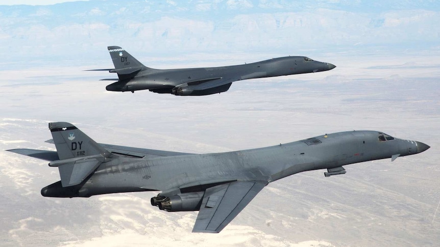 Two B-1B Lancers fly in formation over arid terrain.