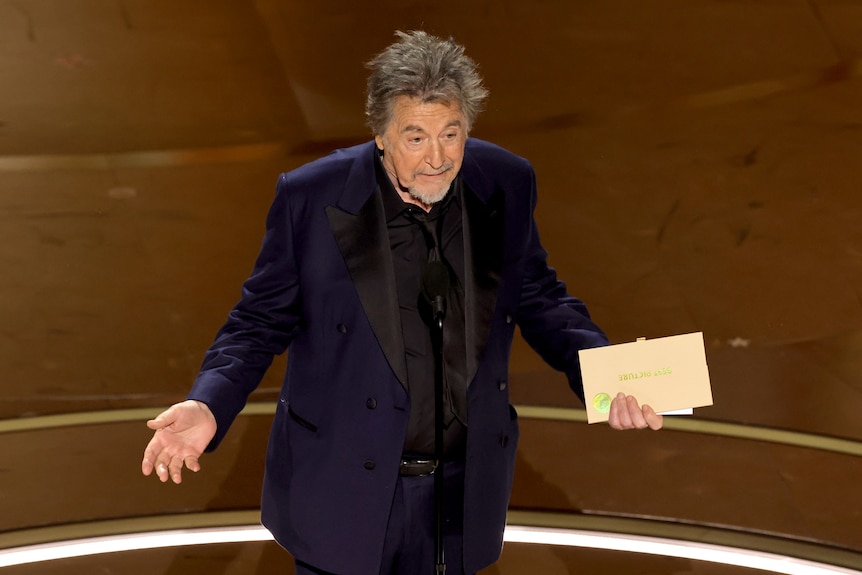 A man in a blue suit holds an envelope in his left hand.