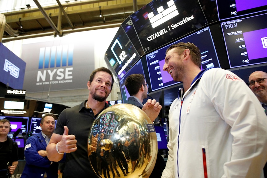 Mark Wahlberg and Adam Gilchrist stand next to the bell on the trading room floor at the New York Stock Exchange