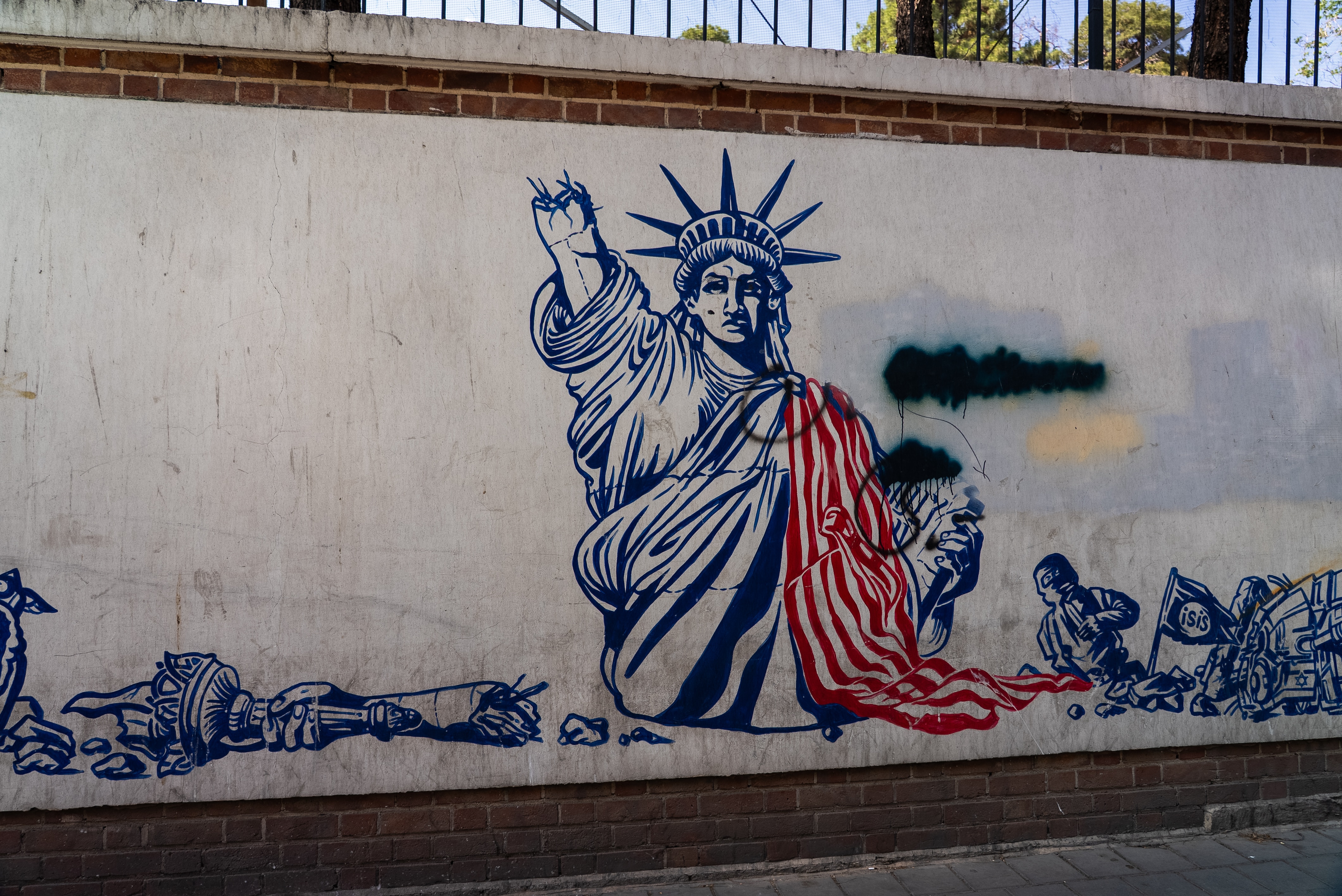 A mural of the Statue of Liberty with her right arm broken off, draped in the US flag in red.