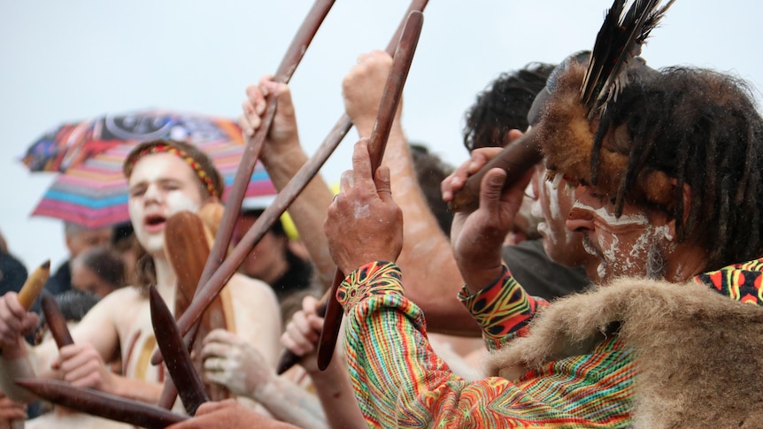 A group of men in traditional attire hold sticks in the air.