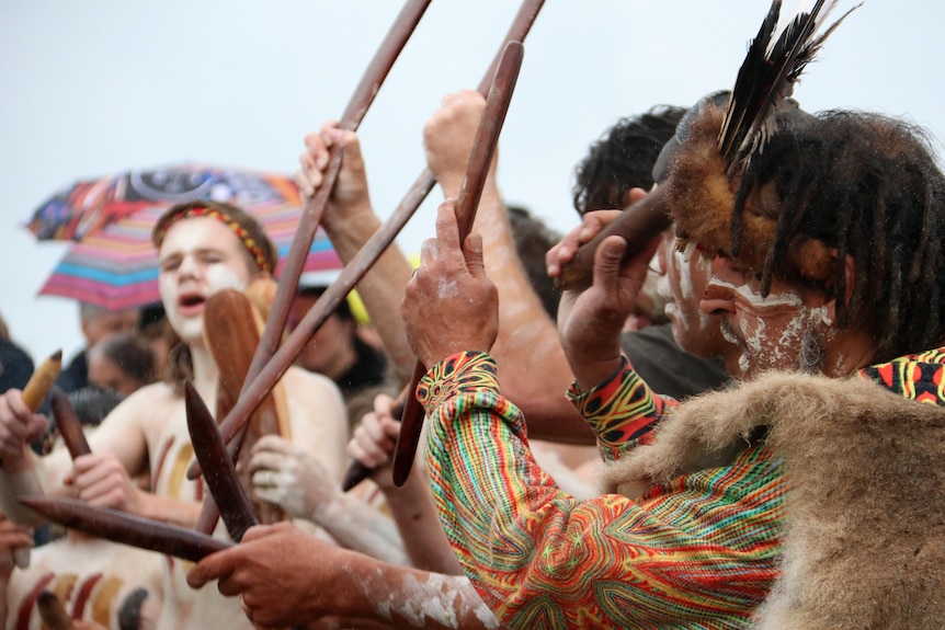 A group of men in traditional attire hold sticks in the air.