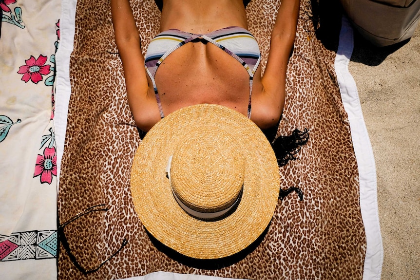 A woman lies on a beach with a sunhat over her face