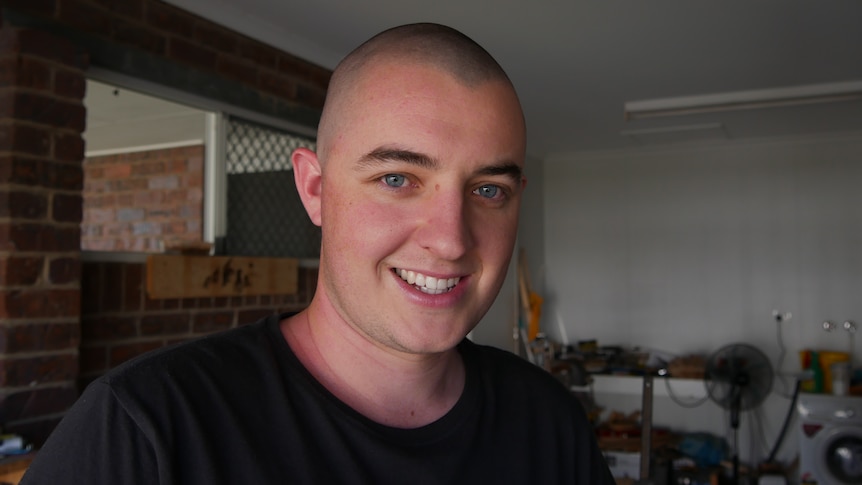 A young man with a shaved head smiles. 