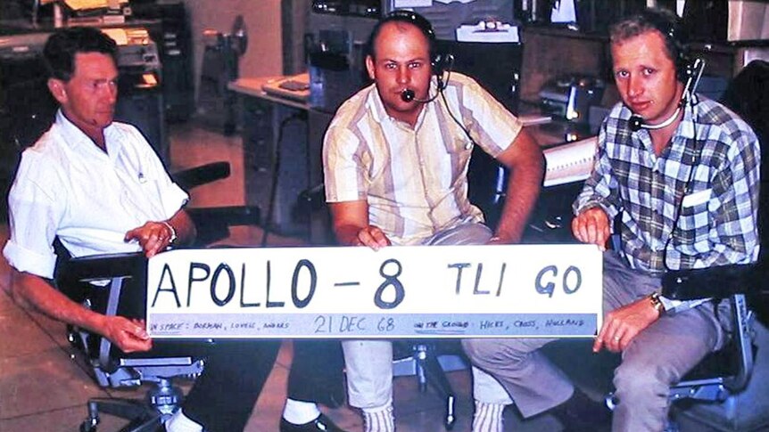 Three men holding a banner saying 'Apollo 8 TLI go'