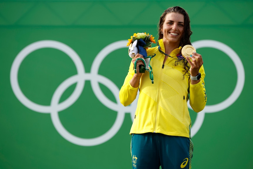 An Australian female kayaker stands with her Olympic gold medal on the podium.