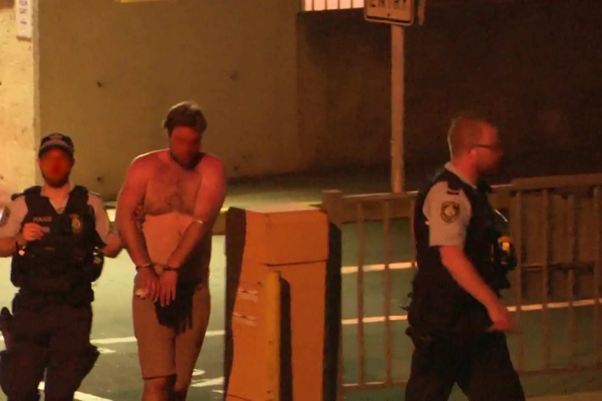 A man flanked by police officers leaves hospital