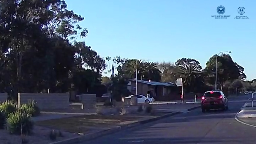 A suburban street with a red car driving on it, with a white Toyota Camry sedan on a side street