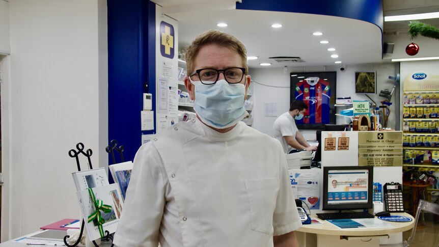 A chemist wearing a face mask, near a customer service counter.