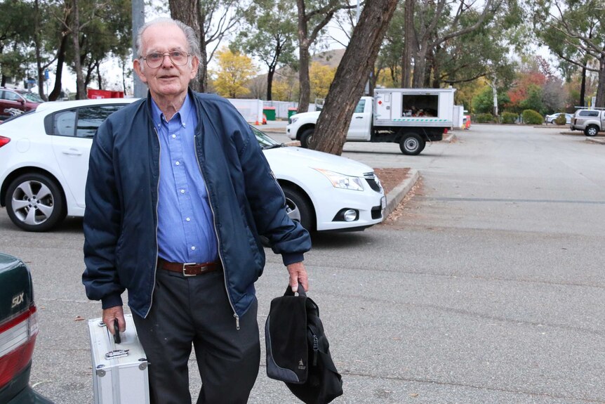 Tony Jones arrives for work in a Tuggeranong car park carrying a suitcase and bag.