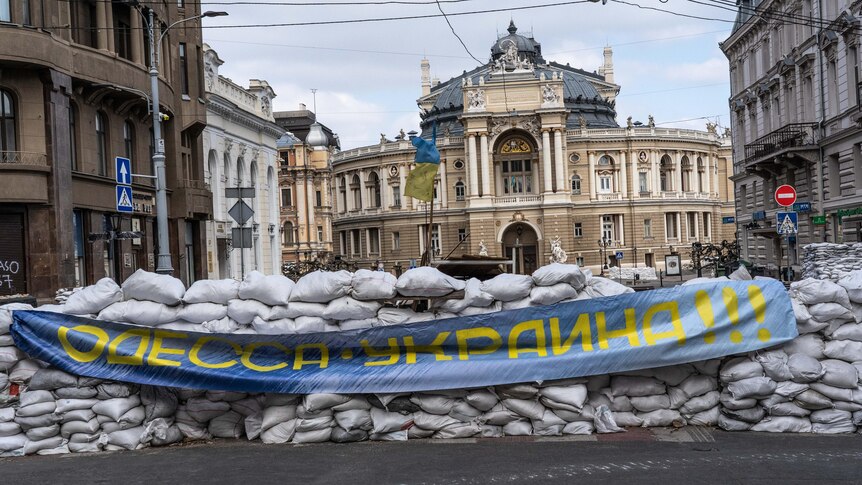 A wall of sandbags lined up on a street with a blue and yellow flag.