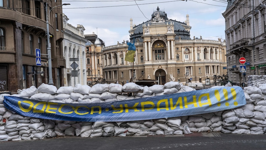 A wall of sandbags lined up on a street with a blue and yellow flag.
