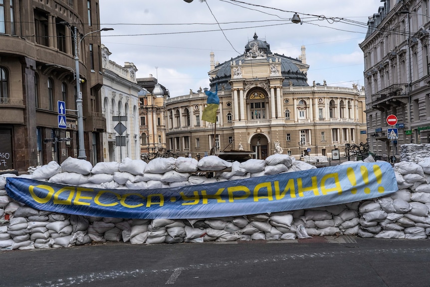 A wall of sandbags lined up on a street with a blue and yellow flag.