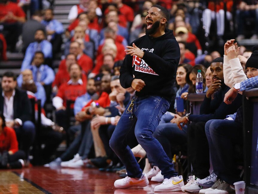 Drake closes his eyes and screams with his hands bent in front of his body as other spectators look on