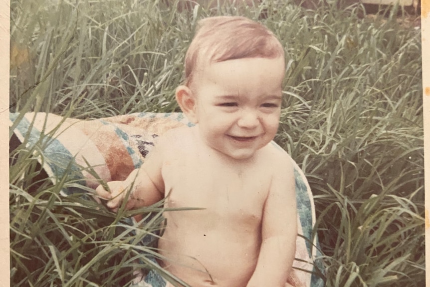 A faded photo of a baby sitting in grass. 