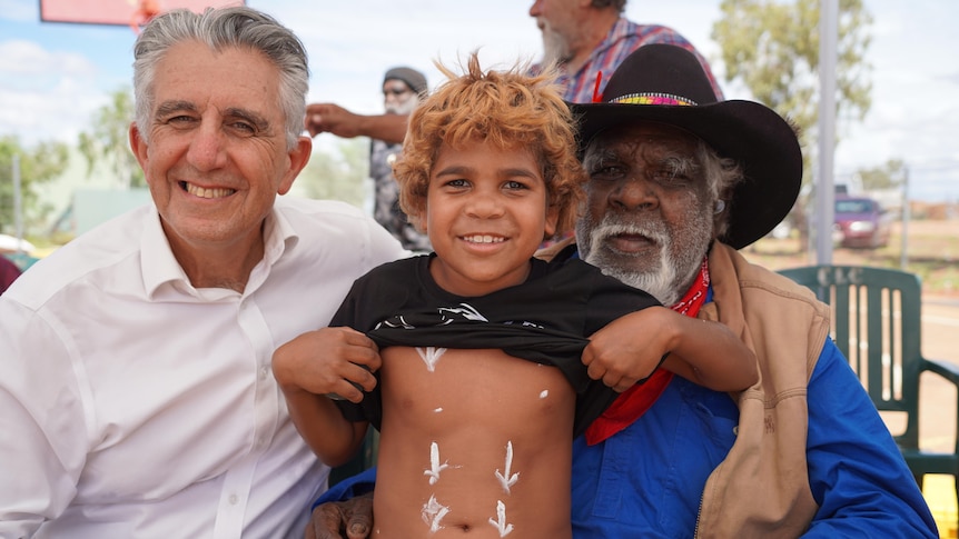 Two men and a child smile in a remote community