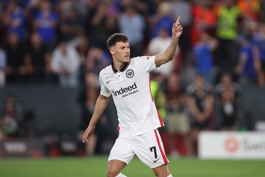 A man in soccer gear points to the sky to celebrate.