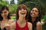 Close-up head and shoulders of three glamorous young women in bikinis smiling as if for the camera.