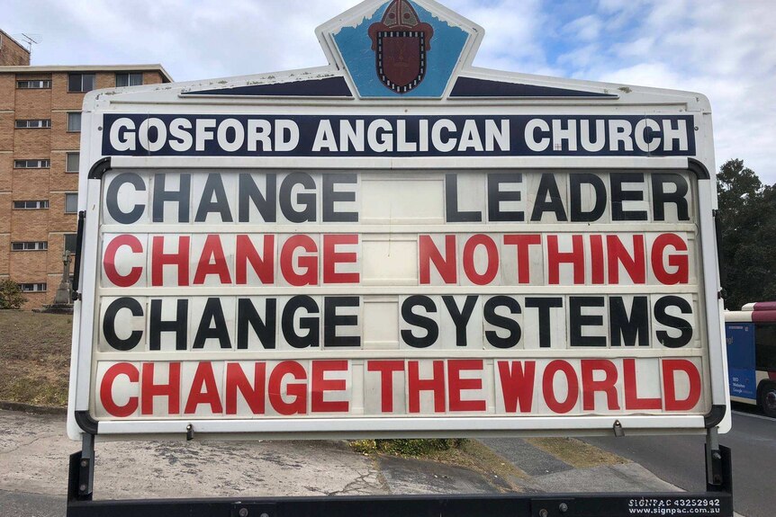 A sign reads, "Change leader, change nothing. Change systems, change the world."