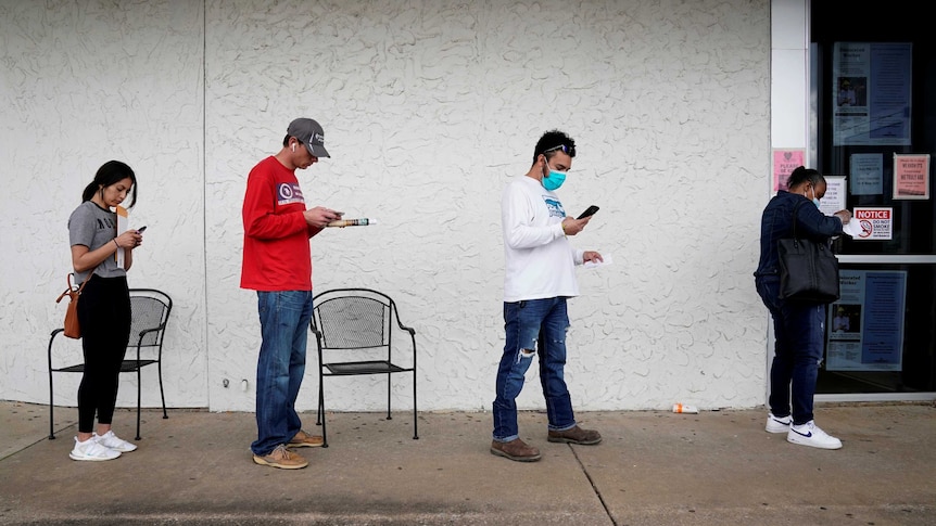 People who lost their jobs wait in line wearing face masks.