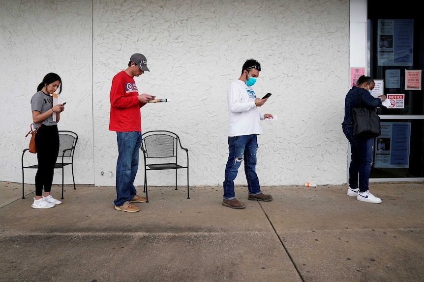 People who lost their jobs wait in line wearing face masks.