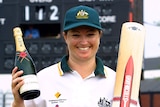 Karen Rolton holds a bottle of Moet champagne in one hand and her cricket bat in the other and smiles.