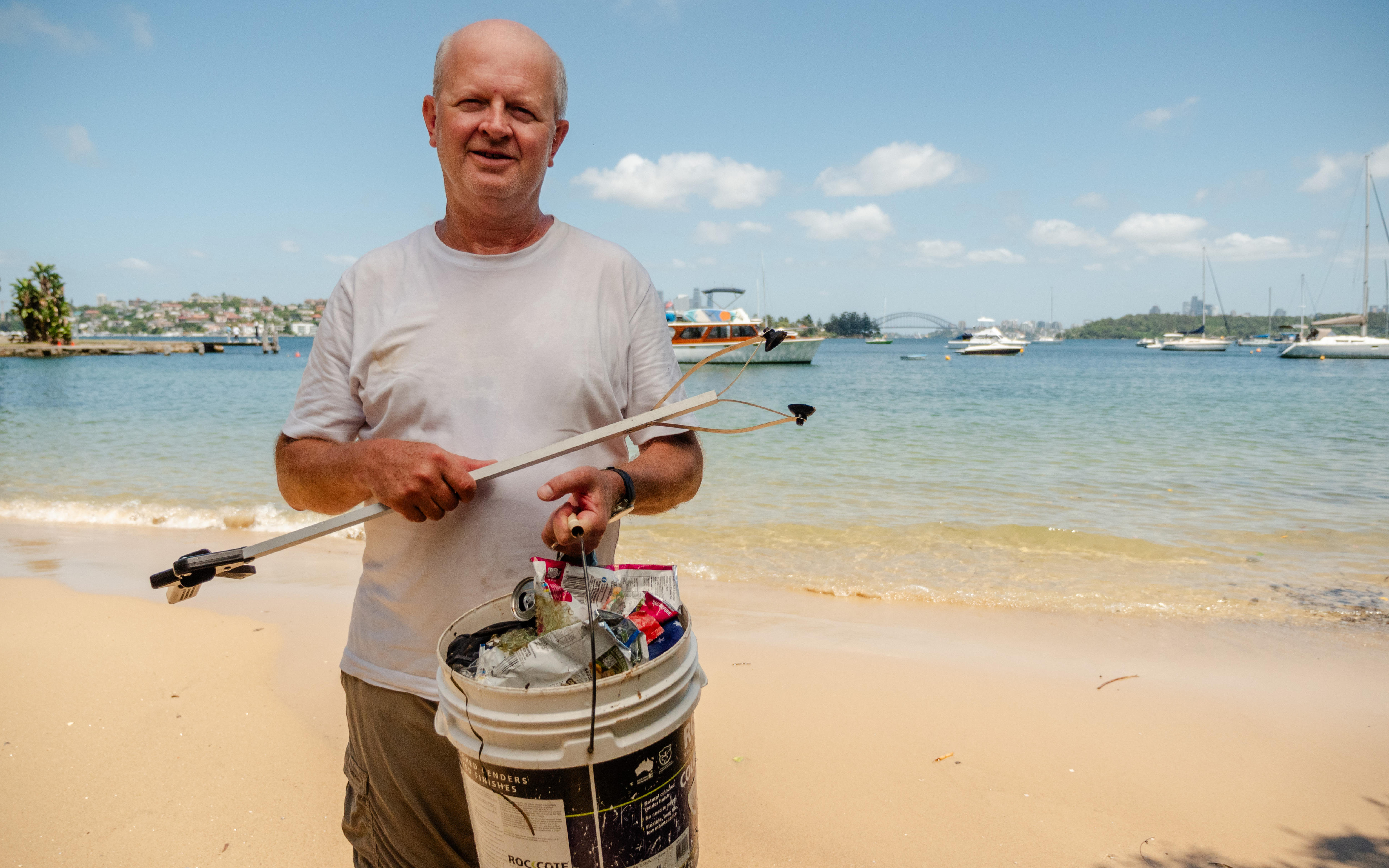 A man standing in Sydney Harbour holding a bucket filled with plastic