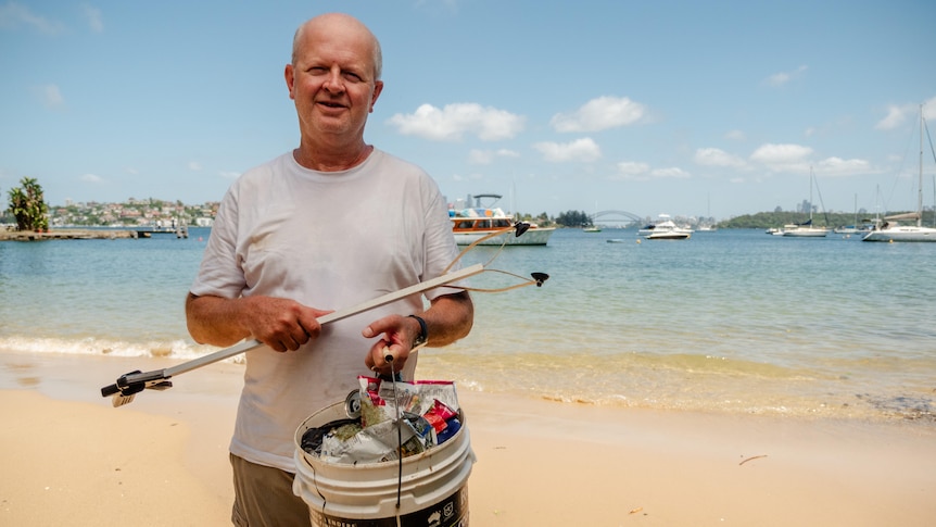 A man standing in Sydney Harbour holding a bucket filled with plastic