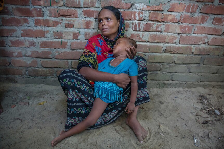 A Rohingya woman holds her emaciated child as she sits in the dirt.