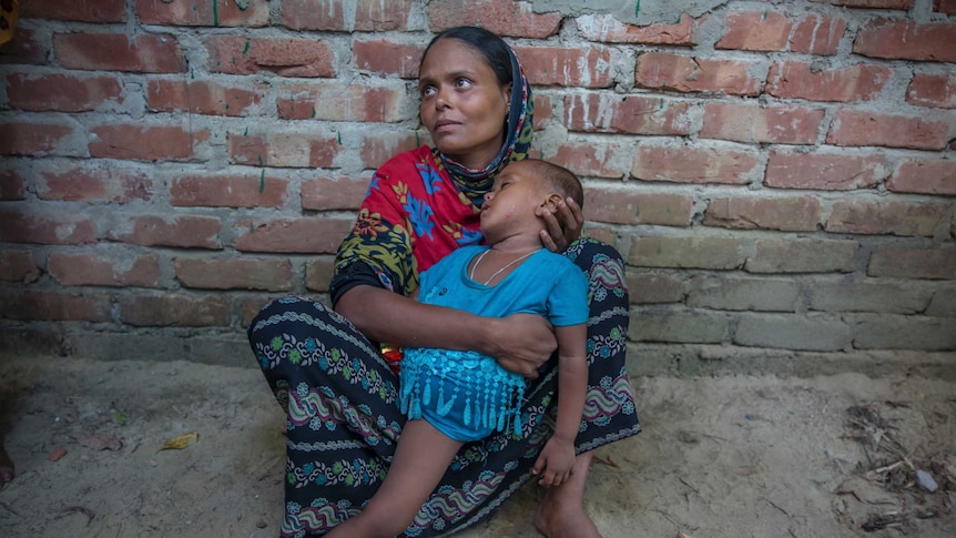 A Rohingya woman holds her emaciated child as she sits in the dirt.