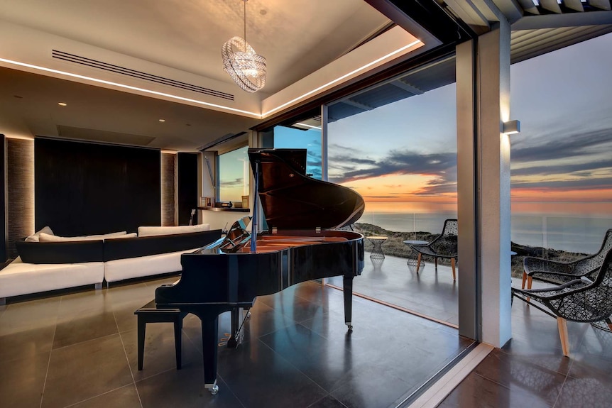 A picture of a grand piano in a living room overlooking the sea