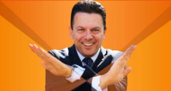 An image of Nick Xenophon smiling with his hands in a cross.