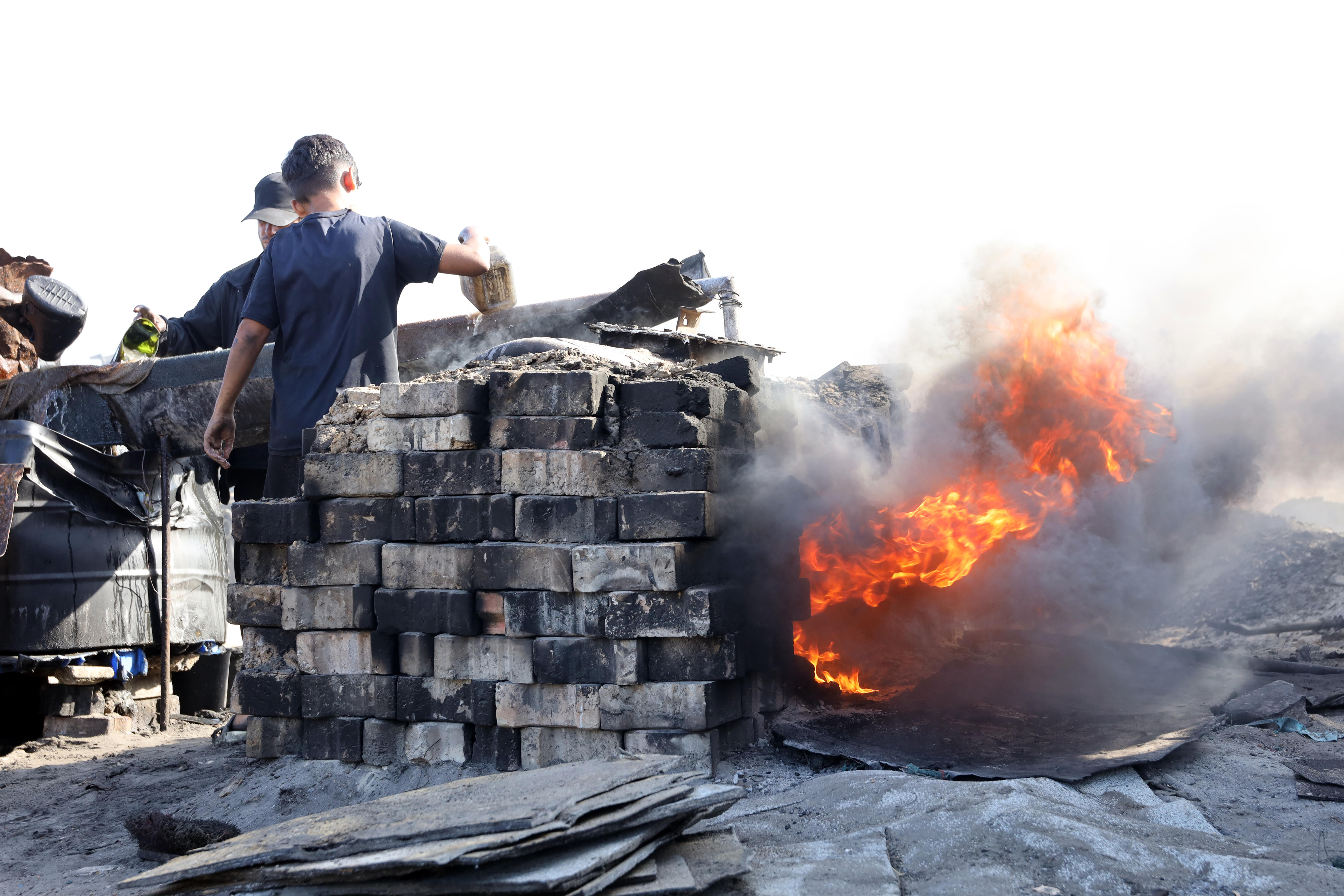 A make-shift brick oven with a large flame burning out the side.