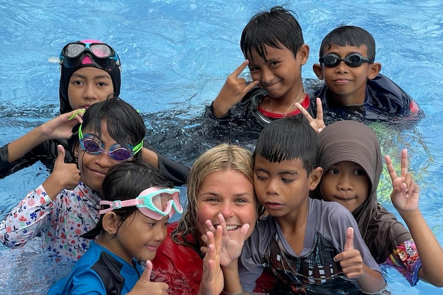 An Australian woman smiling with Indonesian children in a swimming pool.