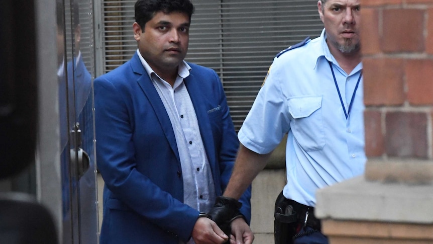 A man in blue suit being taken away in handcuffs