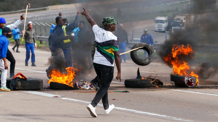 Men move among burning tyres blocking a freeway empty of traffic