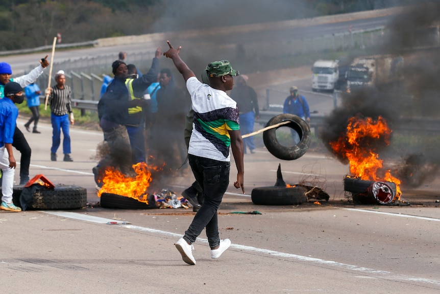 Men move among burning tyres blocking a freeway empty of traffic